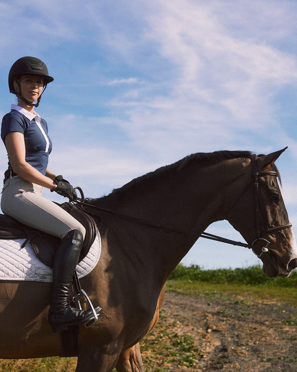 Person riding a horse on a trail with a blue sky and clouds in the background