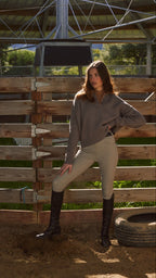 Woman in equestrian attire standing in a stable.