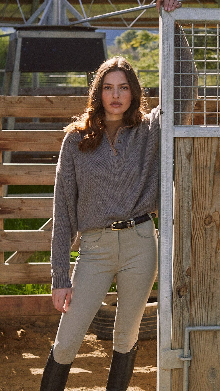 Woman standing in a barn or stable area with wooden stalls and a metal gate.