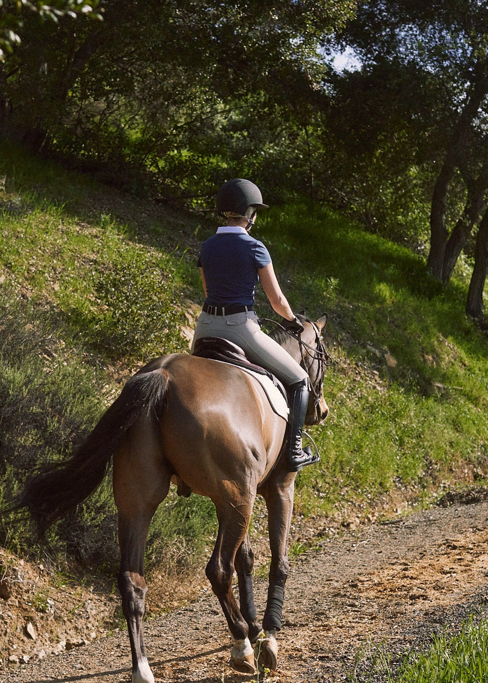 Person riding a horse on a dirt path surrounded by trees